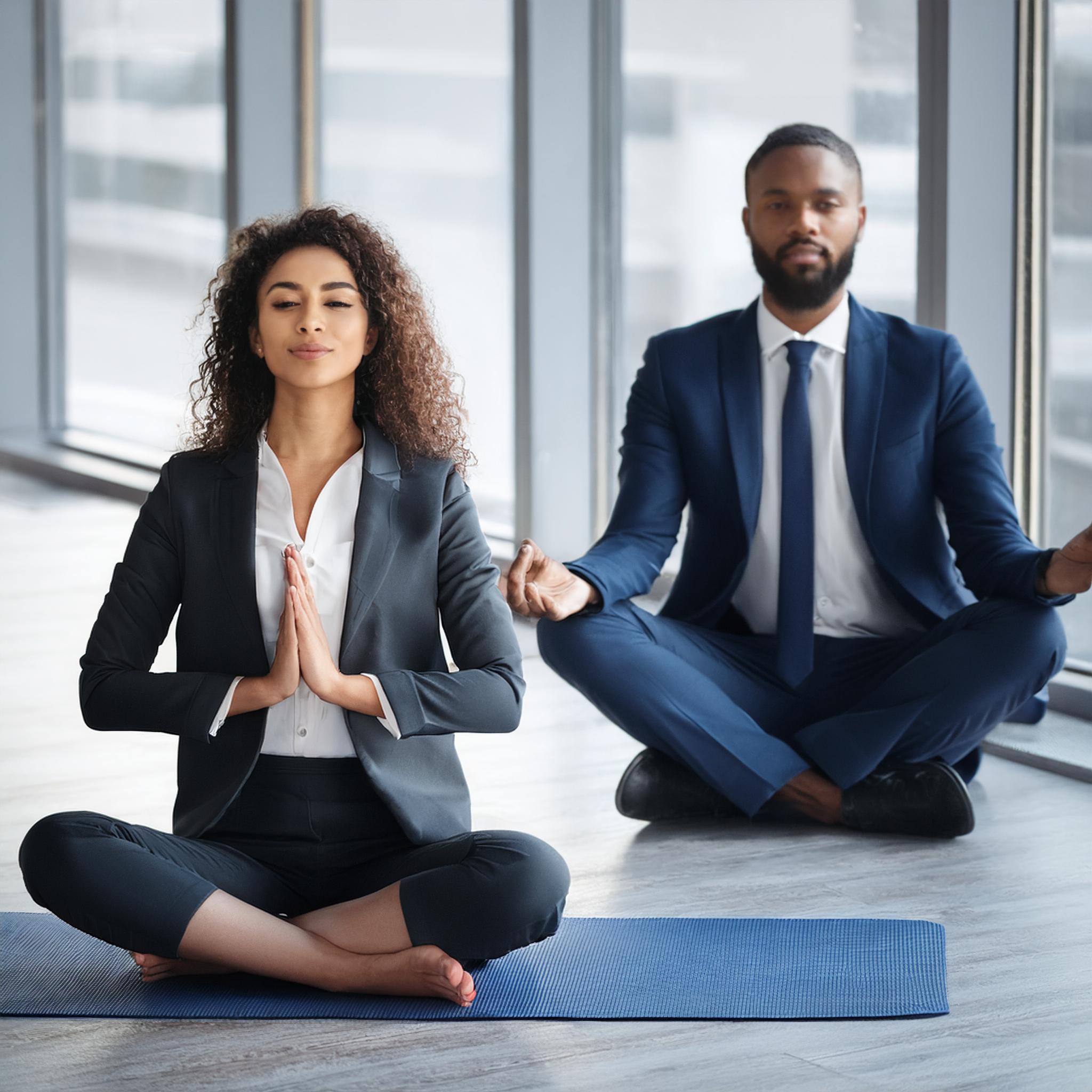 Une femme et un homme employés de bureau se détendent dans une position de Yoga pour illustrer le bien-être au travail